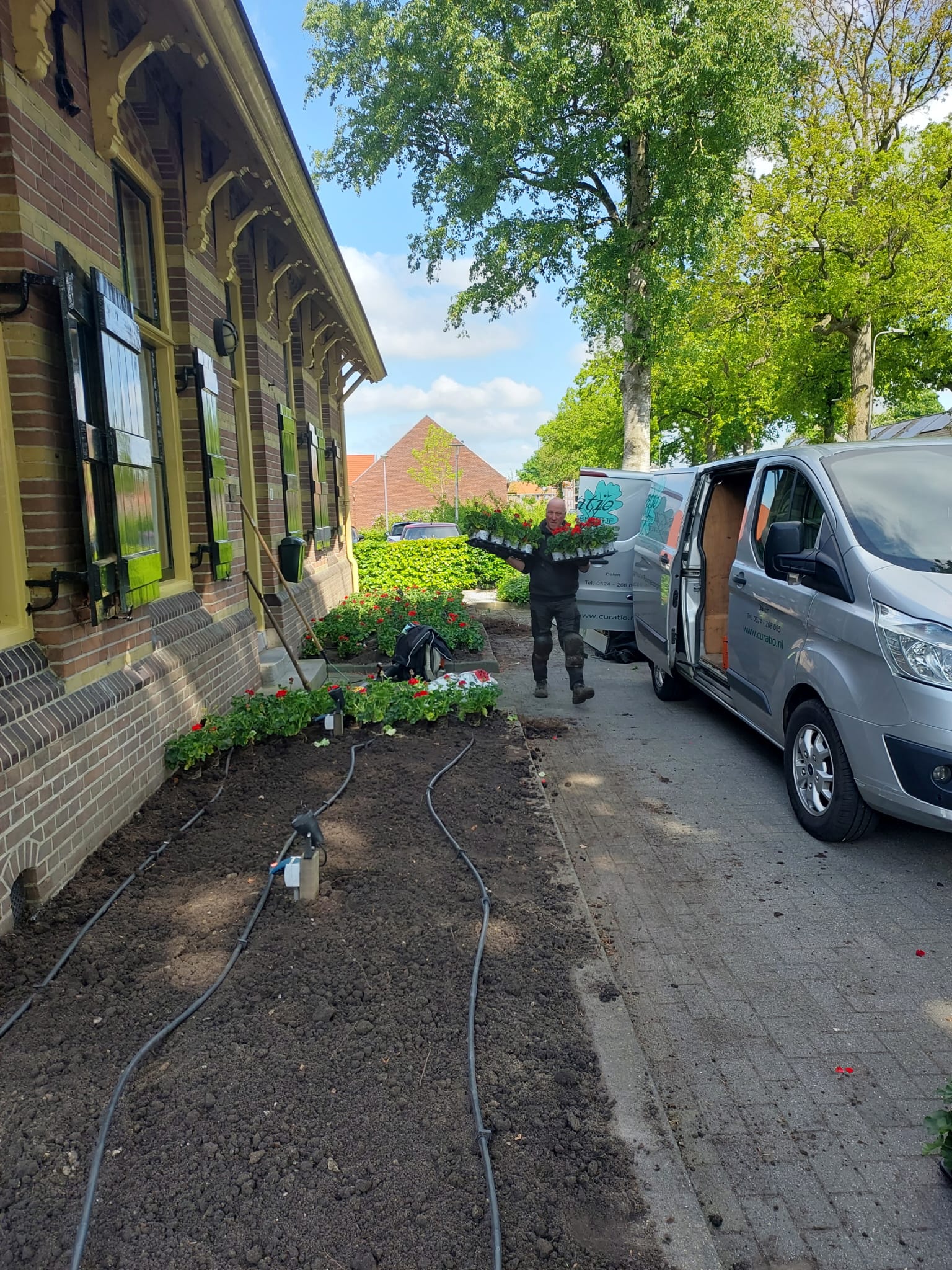 Curatio medewerker met bloeiende planten bij een tuin en bedrijfsbus