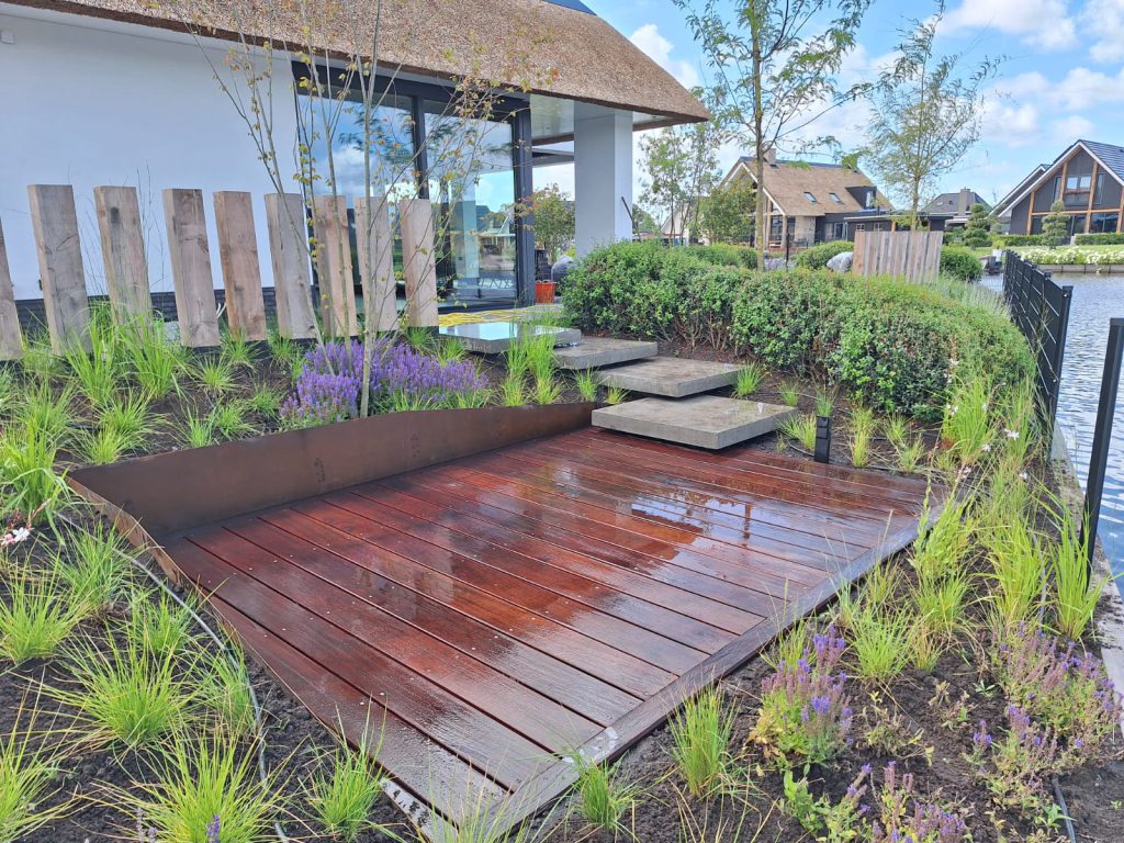 Houten vlonderterras tussen beplanting bij een tuin aan het water