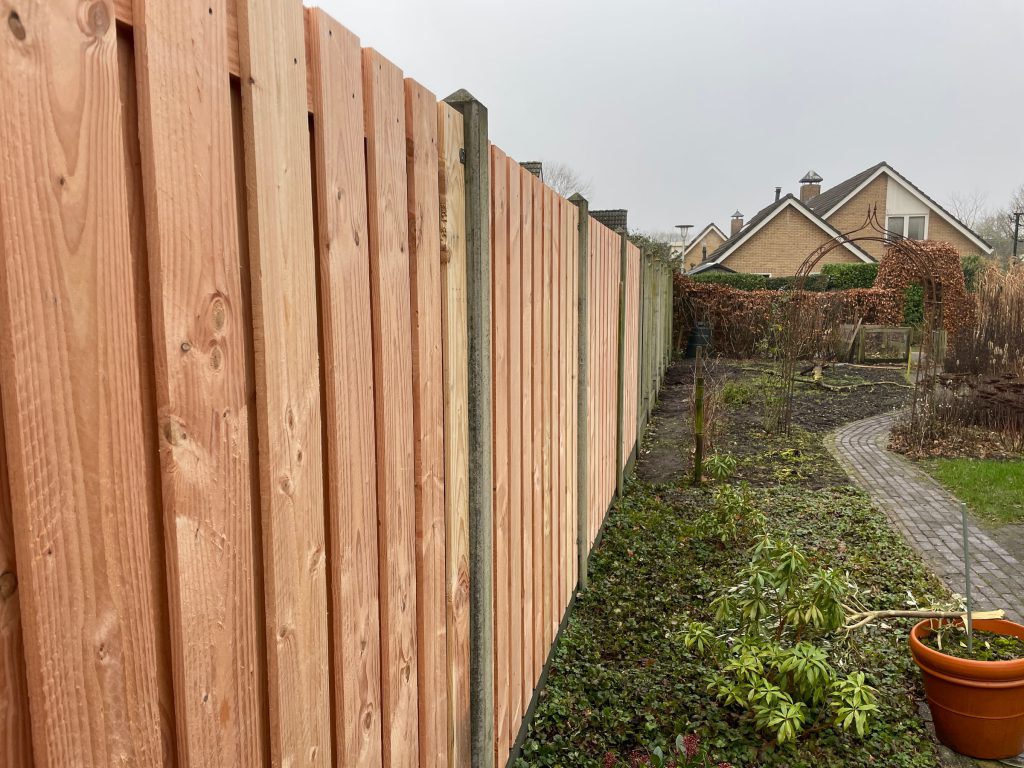 Lange houten schutting met betonpalen langs de tuin