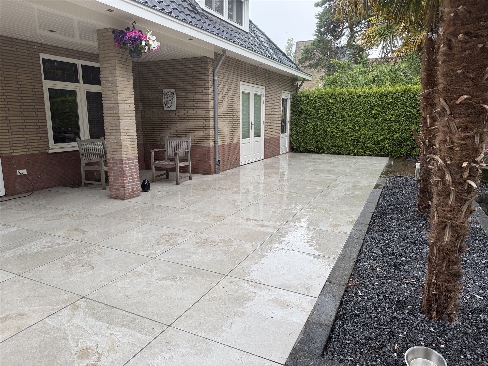 Keramisch terras in Ommen met Varese Greige tegels naast de woning en palmen